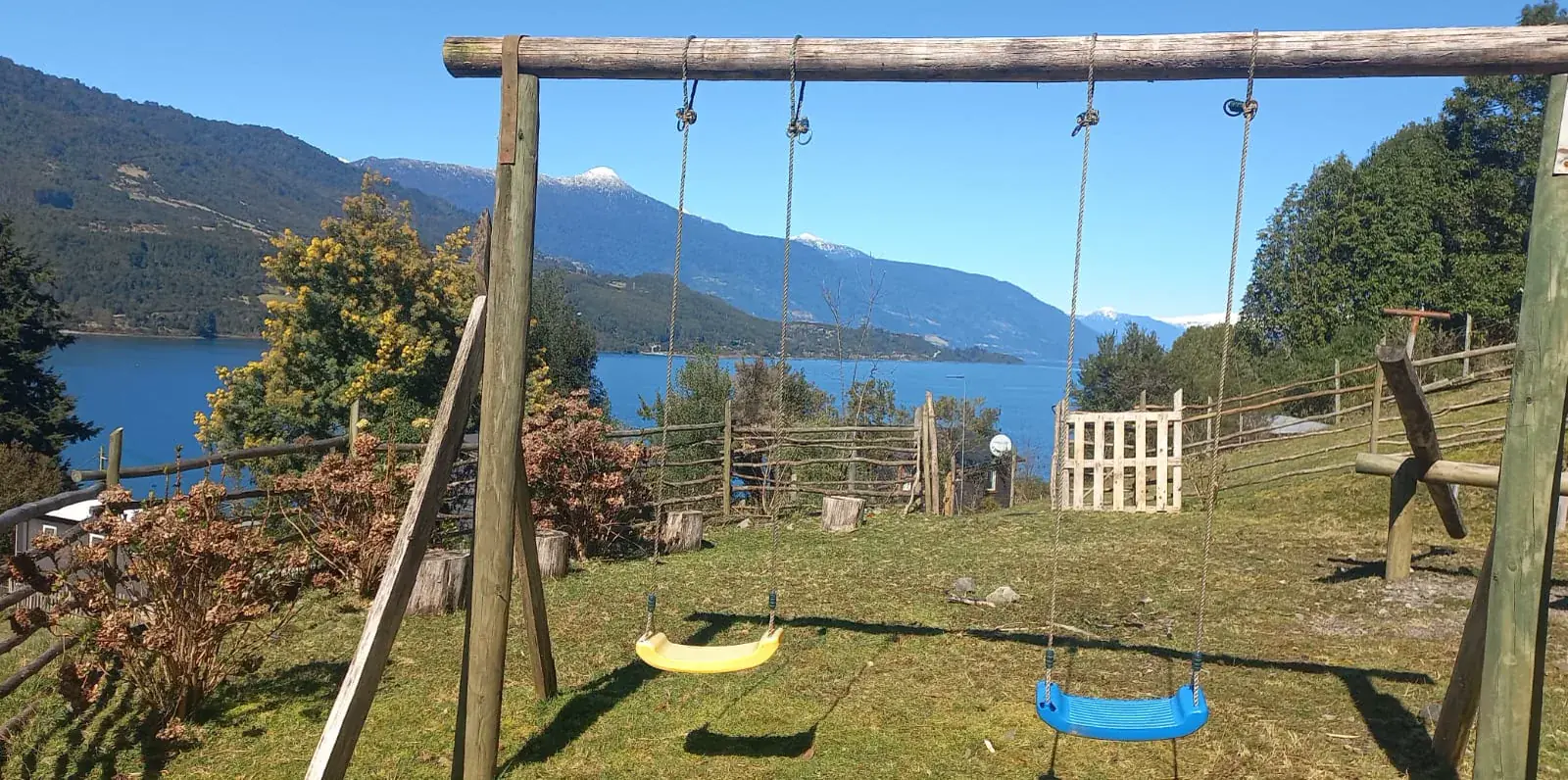 Zona de juegos infantiles con columpios y vista al agua y las montañas
